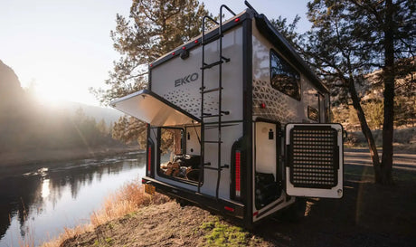 Experience freedom with an RV rental! Rear view of a Winnebago EKKO camper by a river, ready for adventure with open storage.