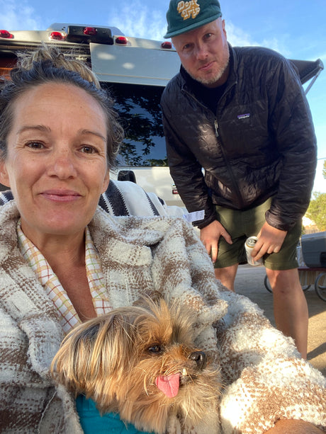Relaxing RV rental journey! A couple and their shaggy dog cozy up with a blanket by their camper van.