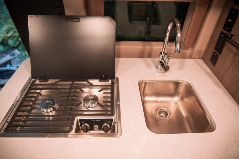 This RV rental features a compact kitchen with a Dometic 2-burner stove and stainless steel sink. — photo 10