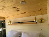 RV rental bedroom features a cozy wooden ceiling, gold reading lamps, and a convenient bedside shelf for van life.