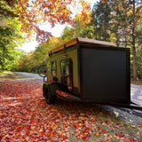 Autumn RV rental adventure! This compact trailer is parked amidst vibrant fall foliage & fallen leaves, perfect for a road trip.