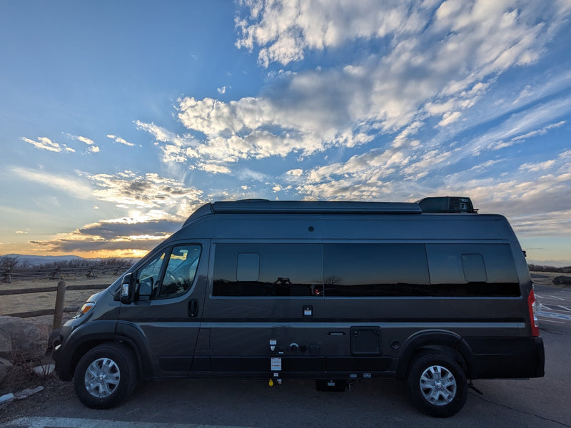 Side view of a dark gray camper van, perfect for an rv rental, parked against a vibrant sunset sky over mountains. — photo 15