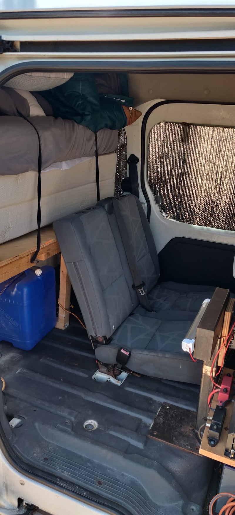 This RV rental's camper van interior features an elevated bed, rear seats, water storage, and an insulated window. — photo 19