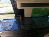 RV rental kitchen with a black speckled counter, stainless steel faucet, and a window overlooking green scenery.