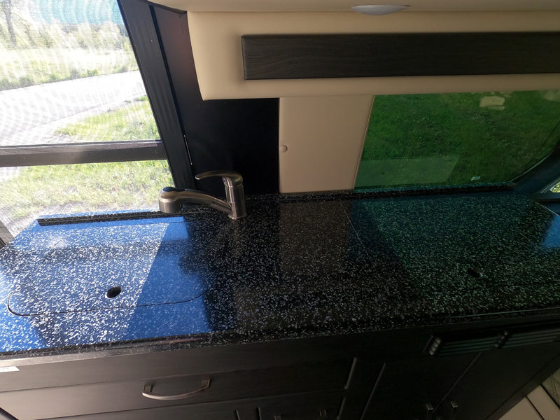 RV rental kitchen with a black speckled counter, stainless steel faucet, and a window overlooking green scenery. — photo 15