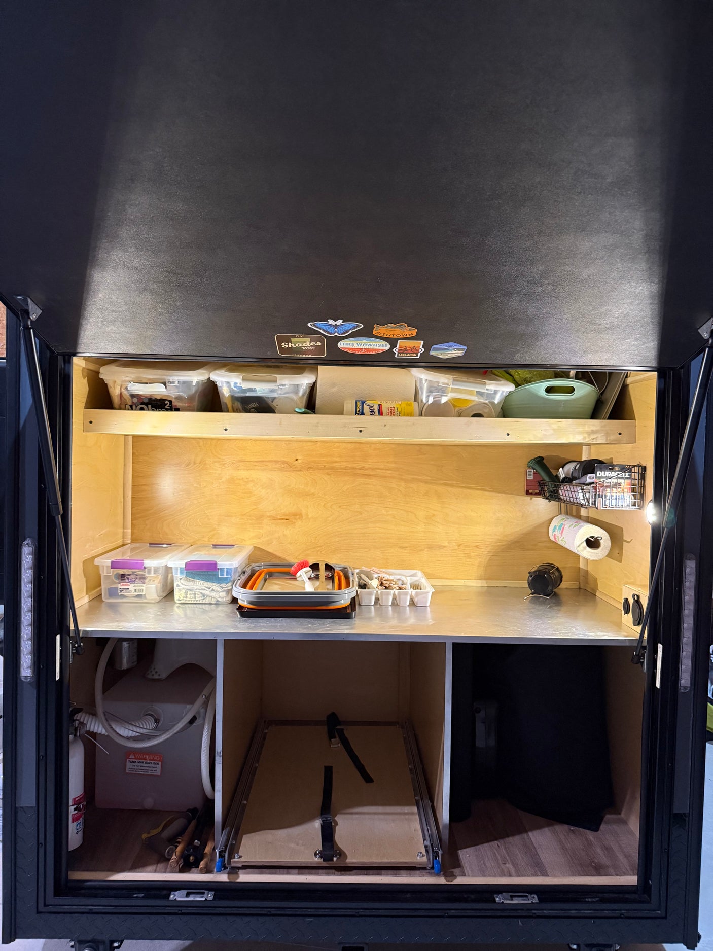Well-organized RV rental rear galley with clear storage, kitchen tools, water tank, and pull-out shelving for camping.