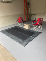 RV rental trip essentials: Two red camping chairs, a tan cooler, and a patterned rug laid out on a light grey garage floor.