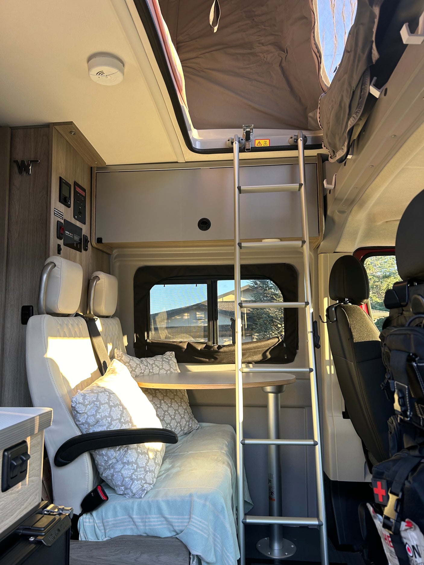 Bright RV rental interior: Ladder to pop-top bed, light-colored seating, and dining table. A cozy camper van.