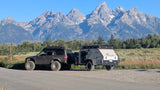 An off-road SUV tows an XTR Venture overland camper trailer, ideal for an RV rental, parked before the majestic Grand Teton mountains.