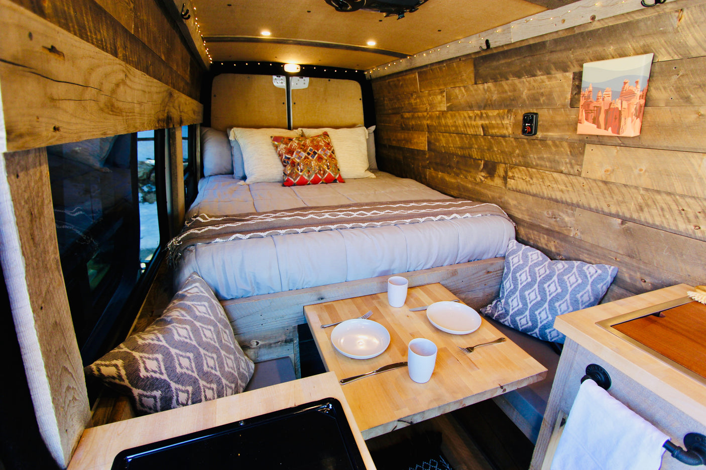 Cozy rv rental interior: a comfortable bed, rustic wooden walls, and a small dining table with place settings. Ideal camper comfort.