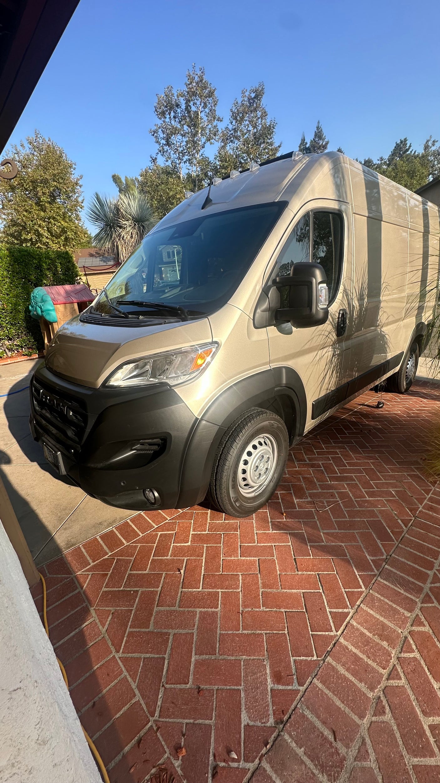 Tan RV rental van parked on a herringbone brick driveway under a sunny sky.