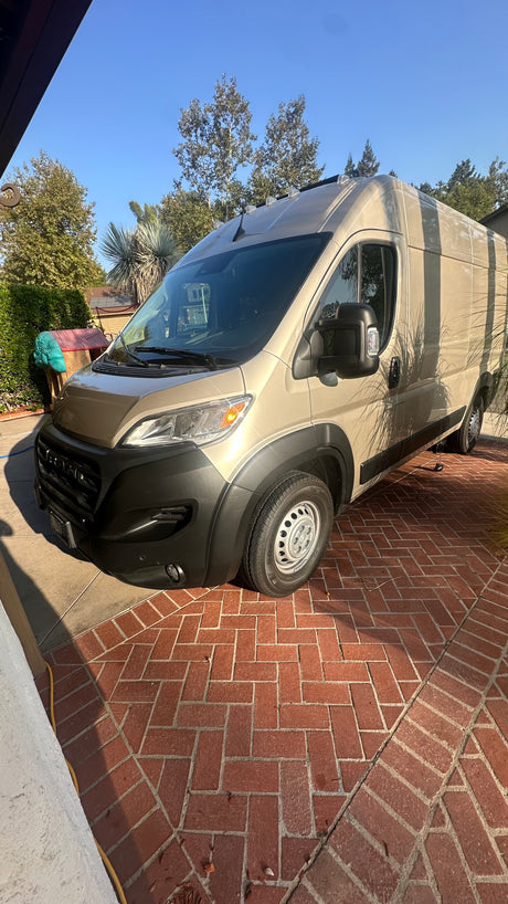Tan RV rental van parked on a herringbone brick driveway under a sunny sky.