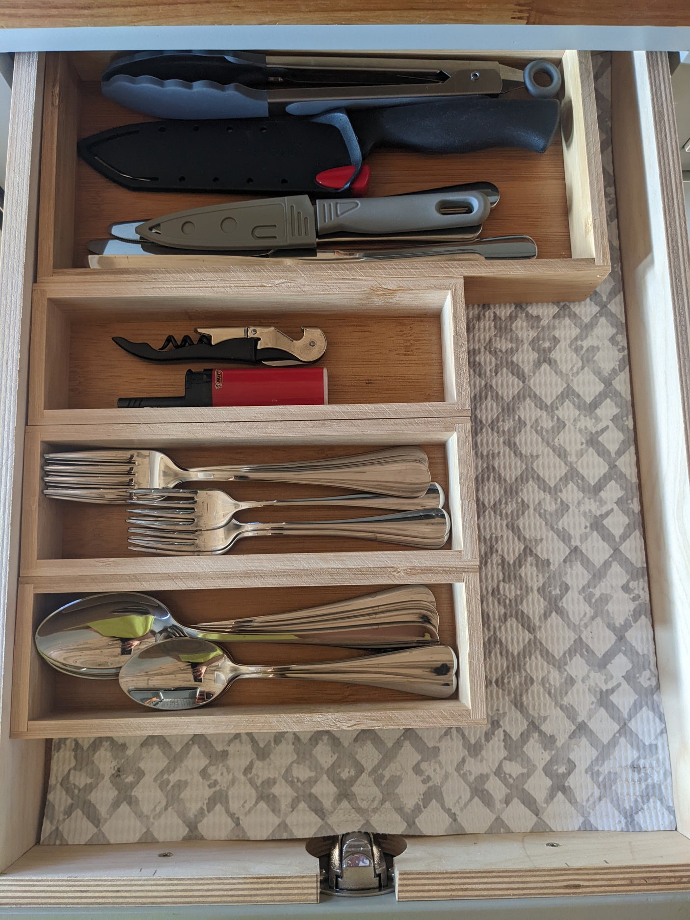An RV rental drawer with kitchen essentials: tongs, knives, corkscrew, lighter, forks, and spoons, neatly organized.