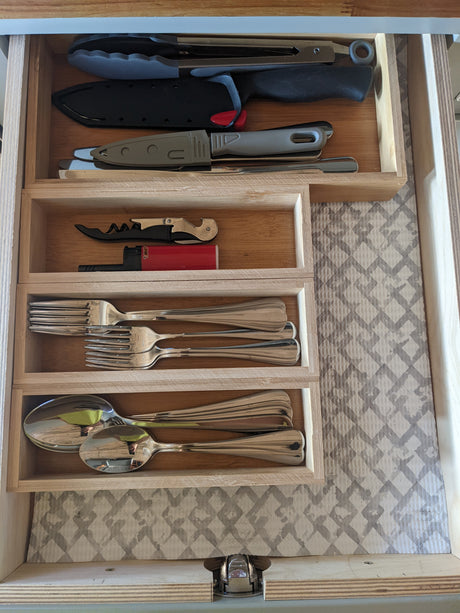 An RV rental drawer with kitchen essentials: tongs, knives, corkscrew, lighter, forks, and spoons, neatly organized.