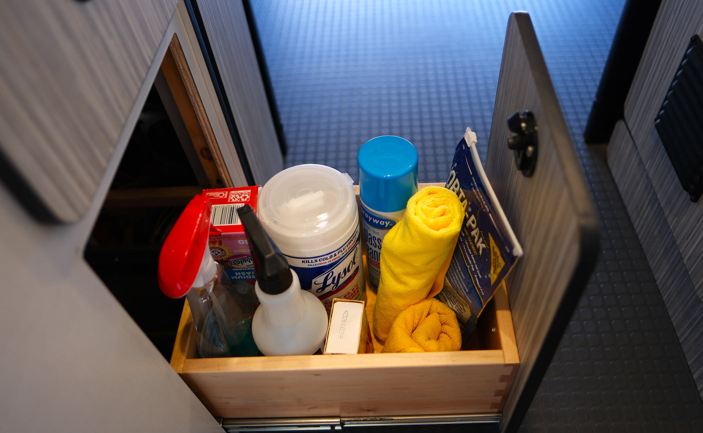 Essential cleaning supplies for an rv rental, like Lysol wipes, glass cleaner, and towels, are organized in a wooden drawer.