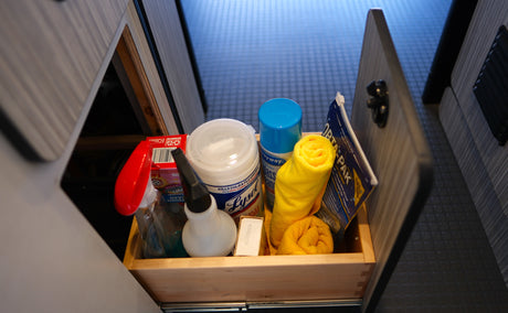 Essential cleaning supplies for an rv rental, like Lysol wipes, glass cleaner, and towels, are organized in a wooden drawer.