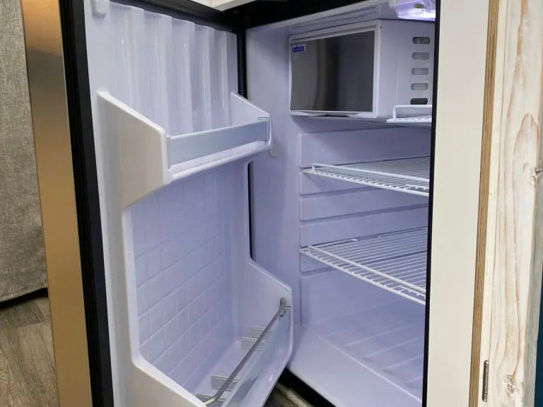 Empty mini-refrigerator inside an RV rental. View shows wire shelves, door storage, and a top freezer, ready for provisions.