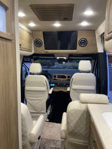 Premium RV rental interior with cream quilted seats, wood accents, TV, and a spacious front cabin view.