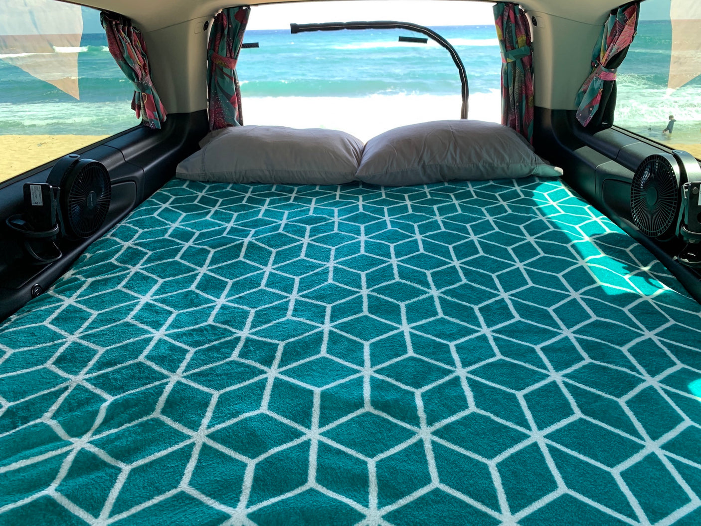 Relaxing RV rental interior with a comfy bed and direct ocean view from the back window, perfect for beach camping.