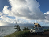 Oceanfront RV rental adventure: A white VW Westfalia camper van with its pop-top open under cloudy skies.