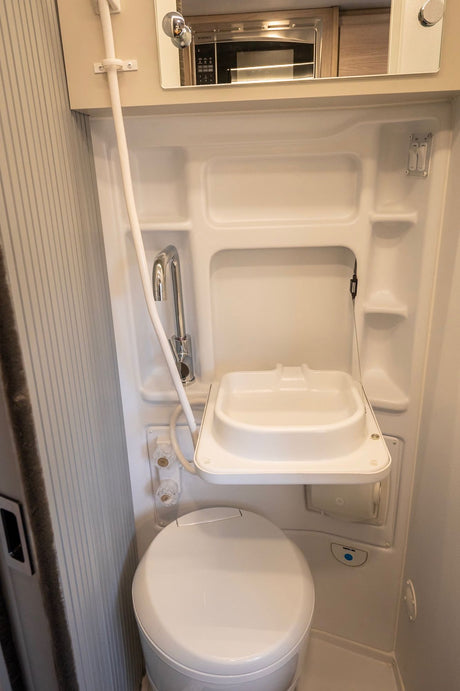 This compact RV rental wet bath features a toilet, fold-down sink, and integrated shower faucet, optimizing space for travel comfort.