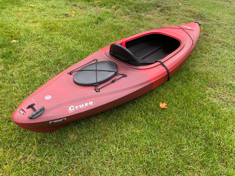 Red kayak on green grass, ready for water adventures. Transport easily with an RV rental.