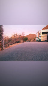 Low-angle desert sunset view: RV rental & car on the road. A fluffy dog's fur is visible on the left, ready for adventure!