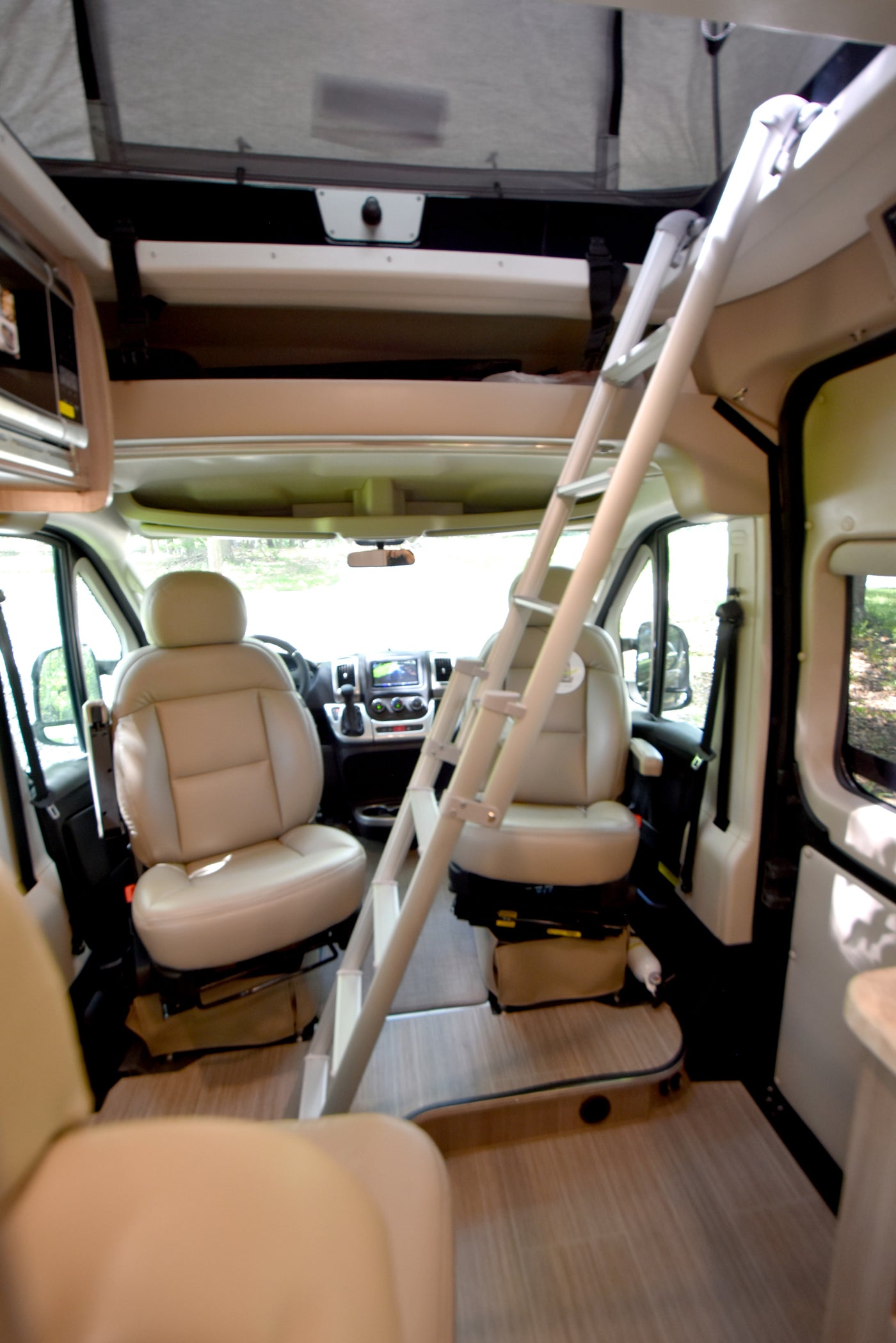 Spacious RV rental interior featuring a ladder to an overhead bunk, with comfortable front cabin seating and dashboard visible. — photo 6