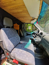 Inside this converted camper van, a wooden ceiling and comfortable seats are visible, along with the dashboard. Ideal for an RV rental.