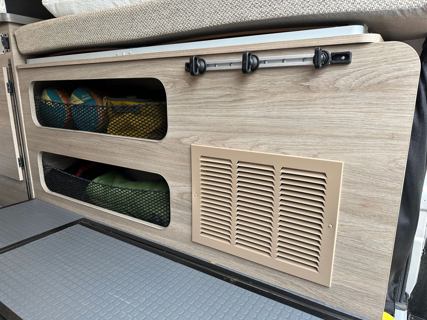 Smart RV rental interior features side storage nets for gear, a lower vent, and bed cushioning above. Practical for camper organization.
