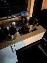 A compact RV rental kitchen features stainless steel pots & pans on a sleek induction cooktop, perfect for mobile cooking.