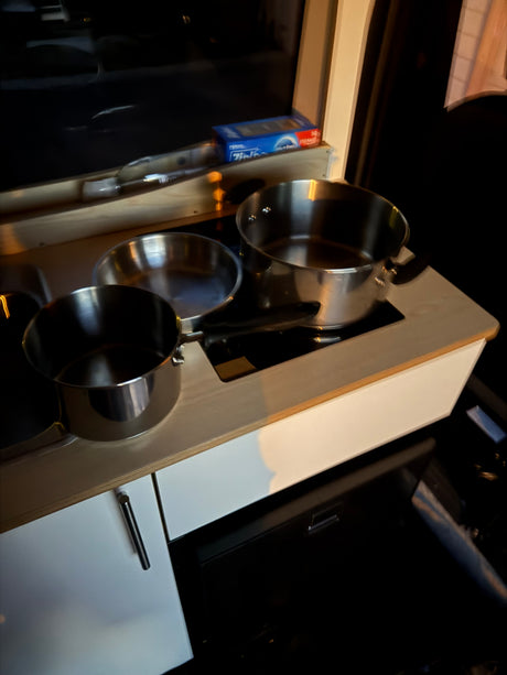 A compact RV rental kitchen features stainless steel pots & pans on a sleek induction cooktop, perfect for mobile cooking.