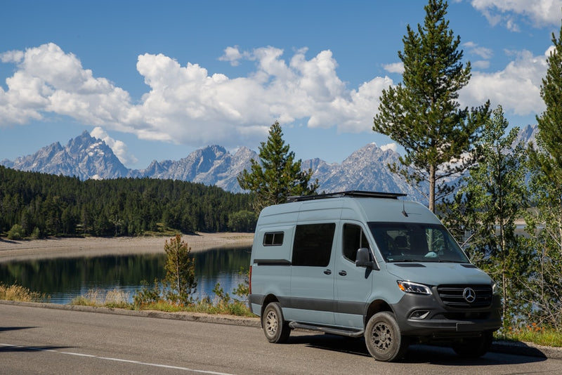  equipped with a bike rack & step.|This light blue RV rental Sprinter van is parked by a scenic lake with majestic mountains under a blue — photo 4