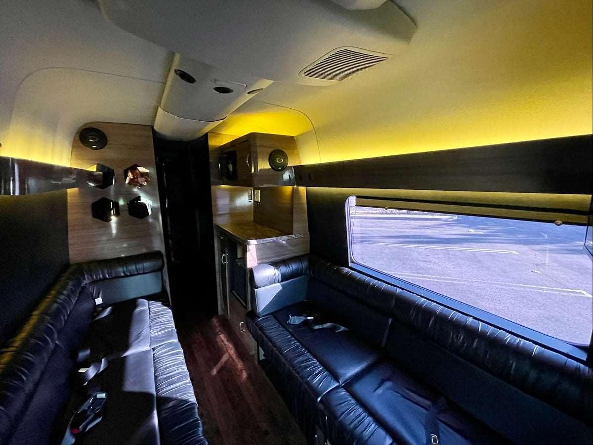 Spacious luxury RV rental interior: black leather couches, warm ambient lighting, wood accents, and a counter area. — photo 4