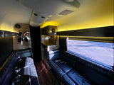 Spacious luxury RV rental interior: black leather couches, warm ambient lighting, wood accents, and a counter area.