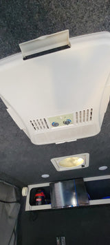 Inside an RV rental: White ceiling-mounted AC unit, roof vent, TV, and vacuum cleaner. Equipped for travel comfort.