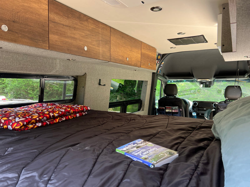 Experience adventure in an RV rental: Interior shows a cozy bed, wooden cabinets, and windows overlooking lush nature. — photo 20