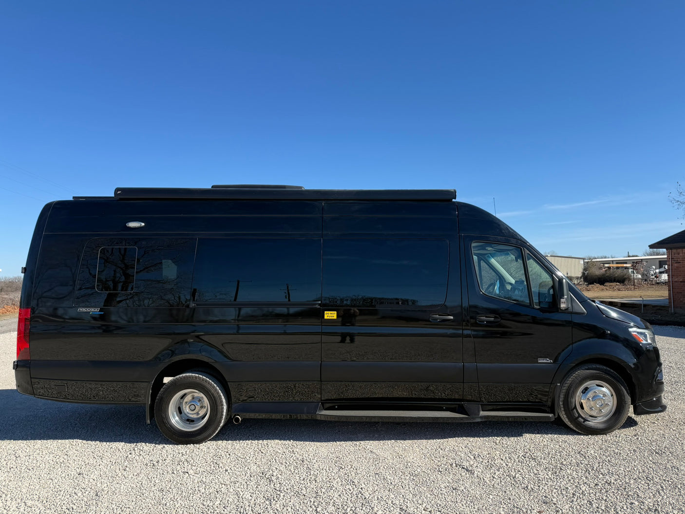 Luxury black rv rental van, a Mercedes-Benz Sprinter, parked on gravel under clear sky. Ideal for road trips and adventure.