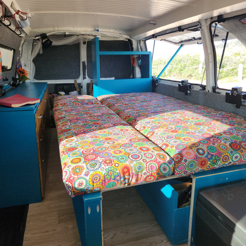 Cozy RV rental interior with vibrant beds, blue storage, and views of nature for comfortable travel. — photo 14