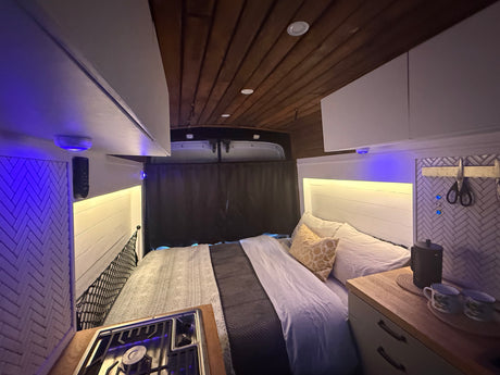 Cozy rv rental camper van interior with a comfy bed, compact kitchen, and inviting ambient lighting.