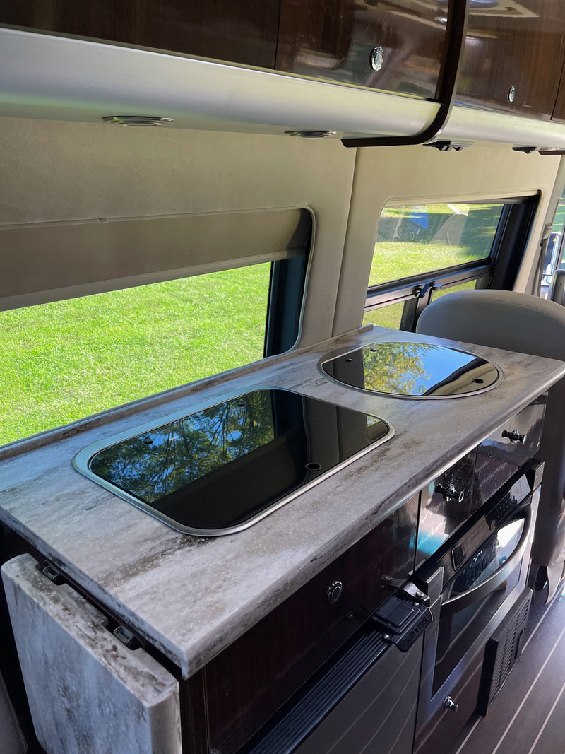 RV rental kitchen interior: modern counter, sink, stovetop, and appliances. Bright view of grass outside. — photo 10