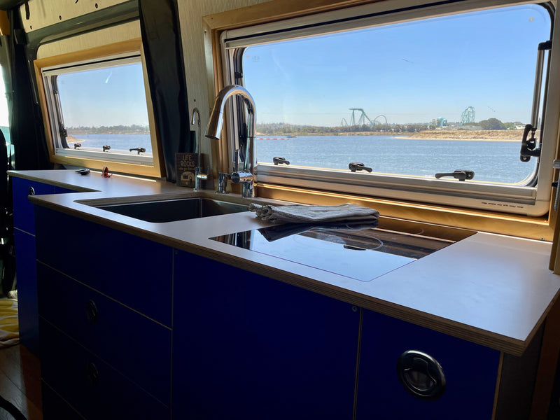 Inside an RV rental: a modern kitchen with blue cabinets, sink, and cooktop, overlooking water and a distant theme park. — photo 4