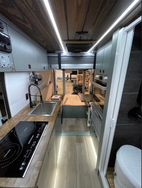 Sleek RV rental interior: kitchen with induction hob, overhead bed, and discreet bathroom. Ready for adventure.