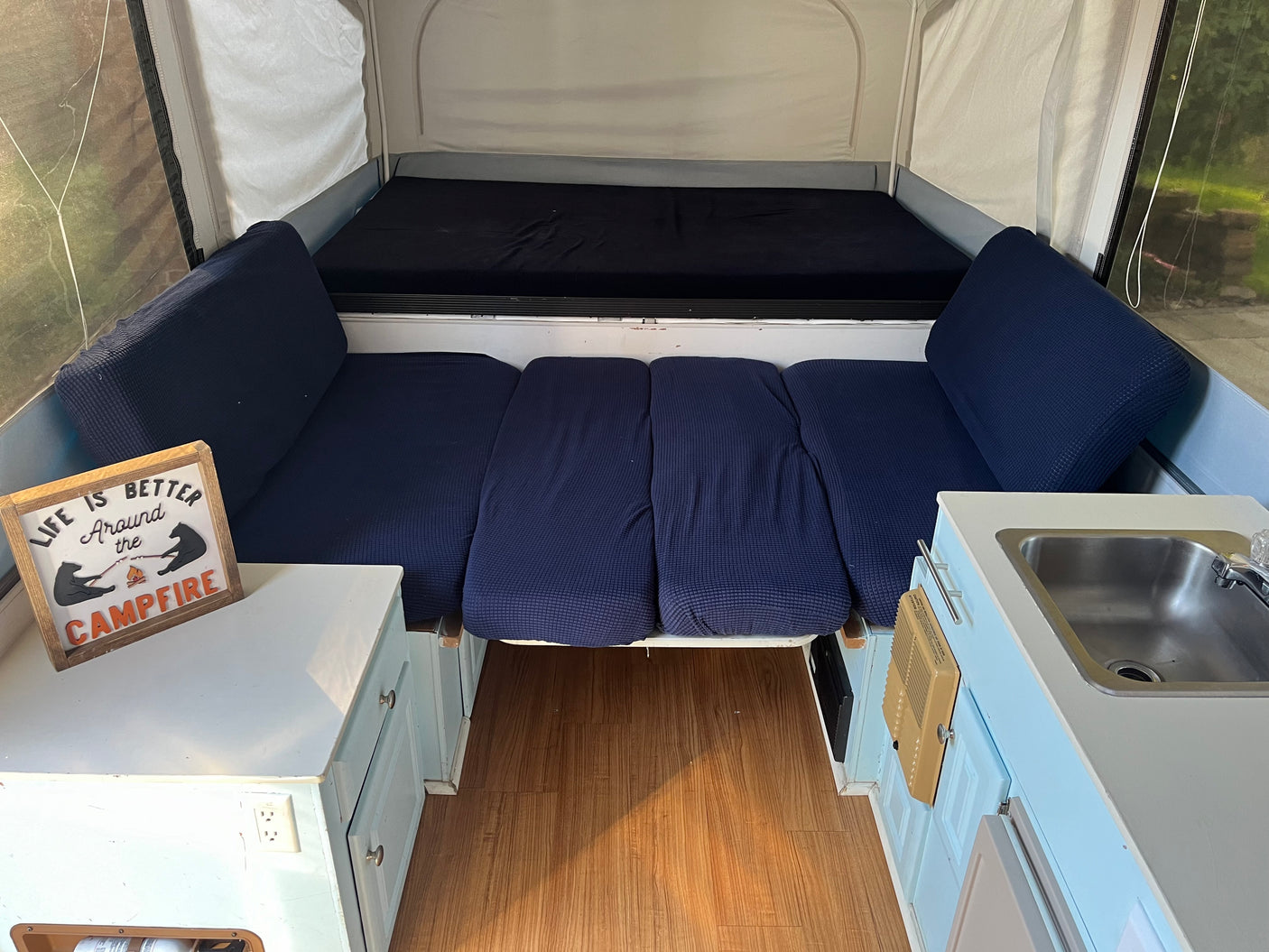 Inside a pop-up RV rental, showcasing blue beds, a compact kitchen sink, wooden floor, and a 'campfire' sign.