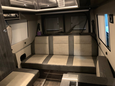 Inside this RV rental: a comfortable lounge area with spacious bench seating, windows, bug screen, and ample storage.