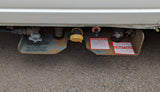 Underside view of an RV rental's LP gas system with propane tank, fill port, and safety labels for safe operation.