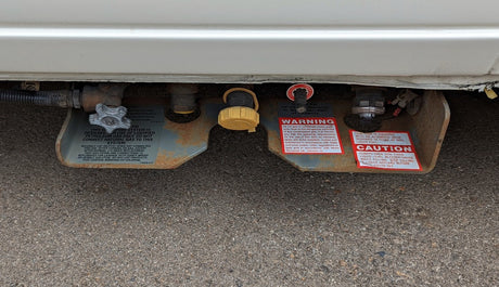Underside view of an RV rental's LP gas system with propane tank, fill port, and safety labels for safe operation.