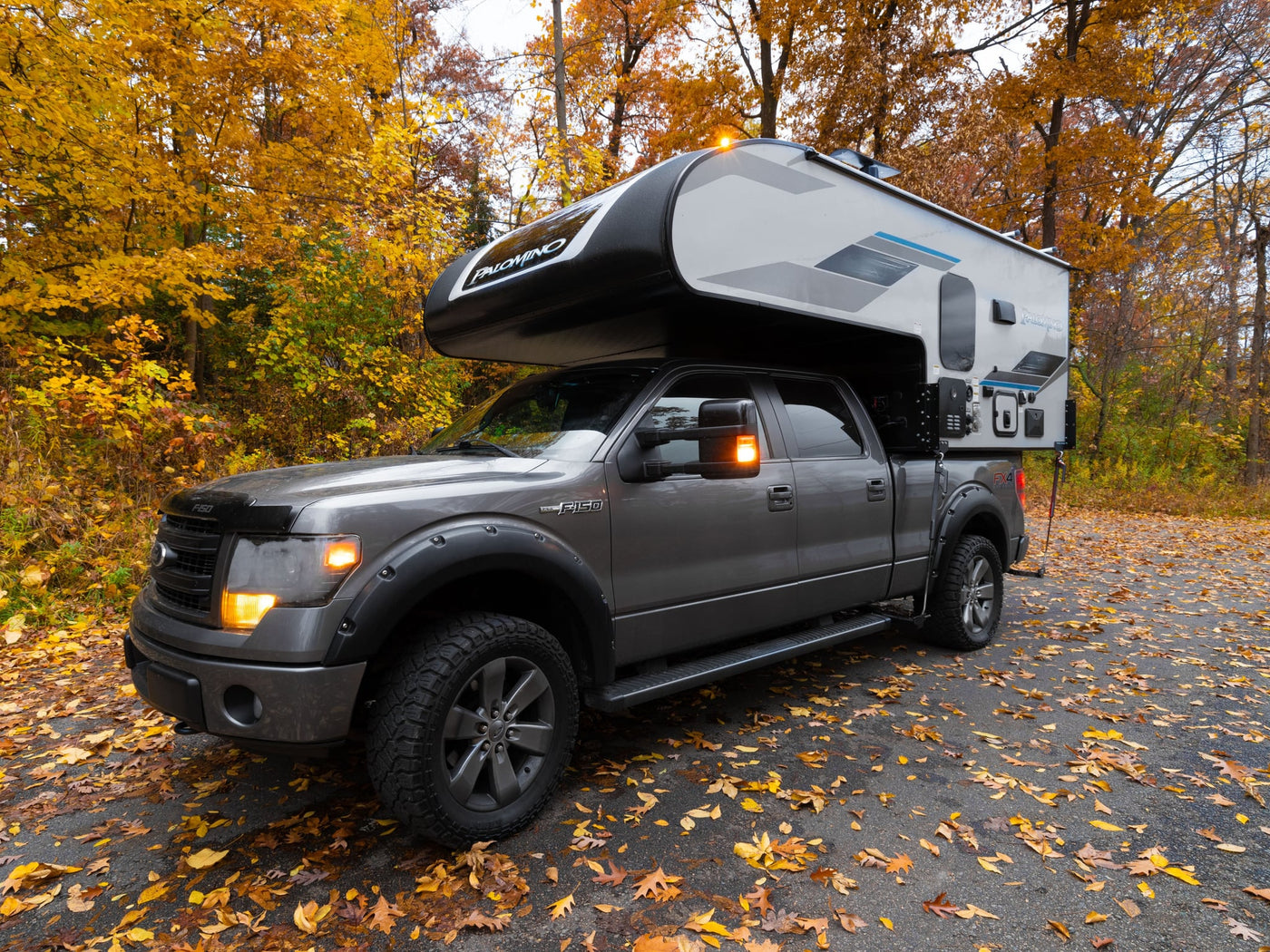  lights on.|RV rental interior: cozy grey seating with a movable wooden table. Window view of colorful fall foliage — photo 4