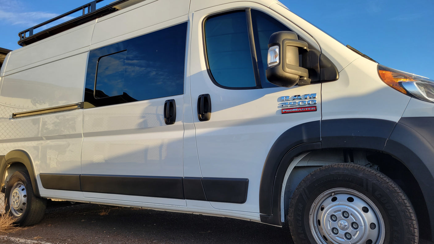 A white Ram ProMaster 2500 campervan, featuring dark windows and a roof rack, perfect for an RV rental.