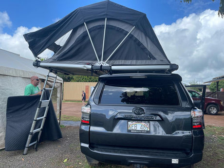Hawaii RV rental: dark SUV with deployed rooftop tent and ladder, ready for camping adventures.